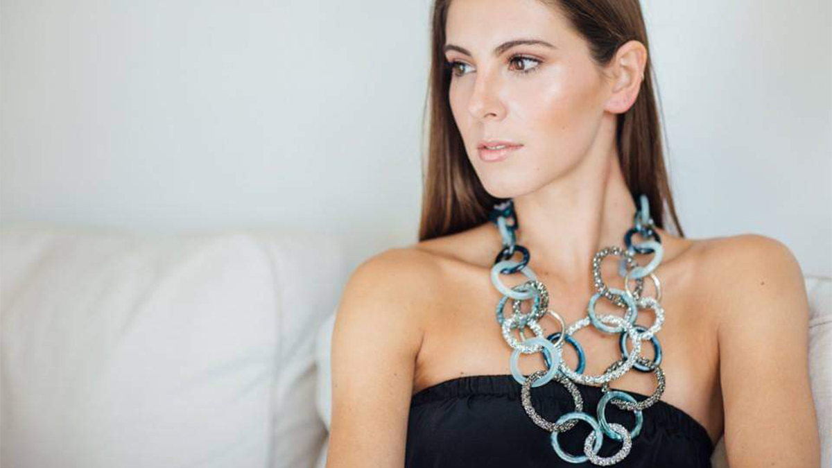 A woman wears a statement piece necklace while sitting on a couch